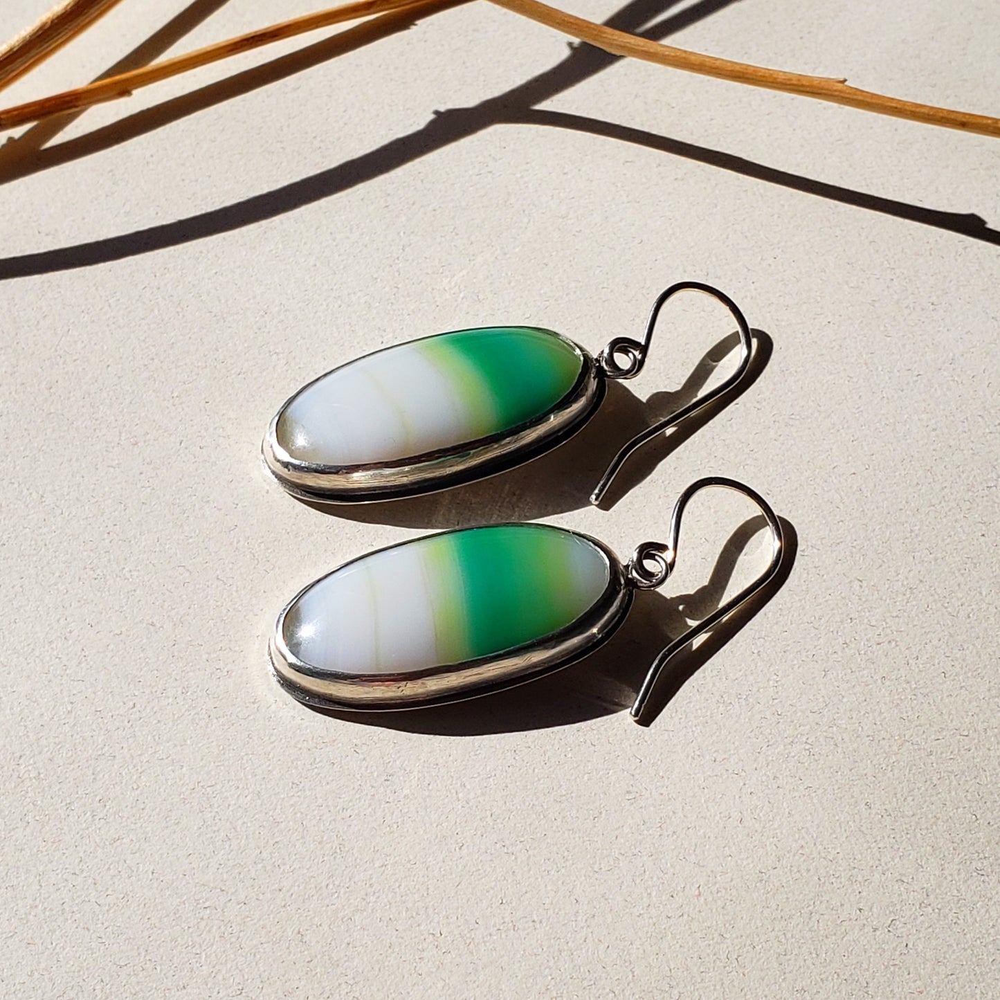 Image of Green and white gemstone statement earrings facing left on tan background