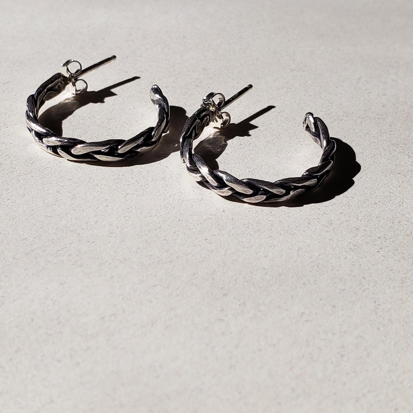 A pair of handcrafted silver hoop earrings against beige background