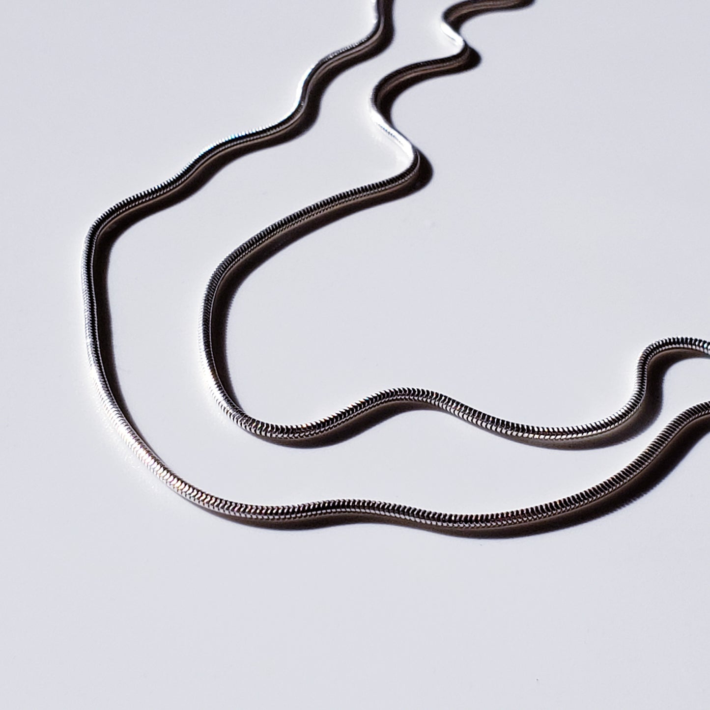 Image of two silver snake chain necklaces on white background