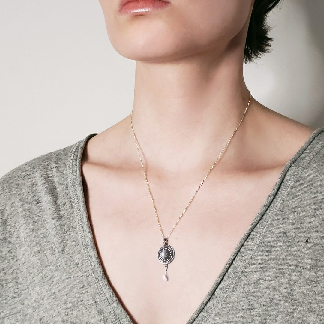 Model wearing a silver and pearl mandala necklace against a white background