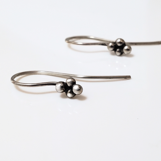 Sterling silver ear wires with four small silver balls laying on white surface board.