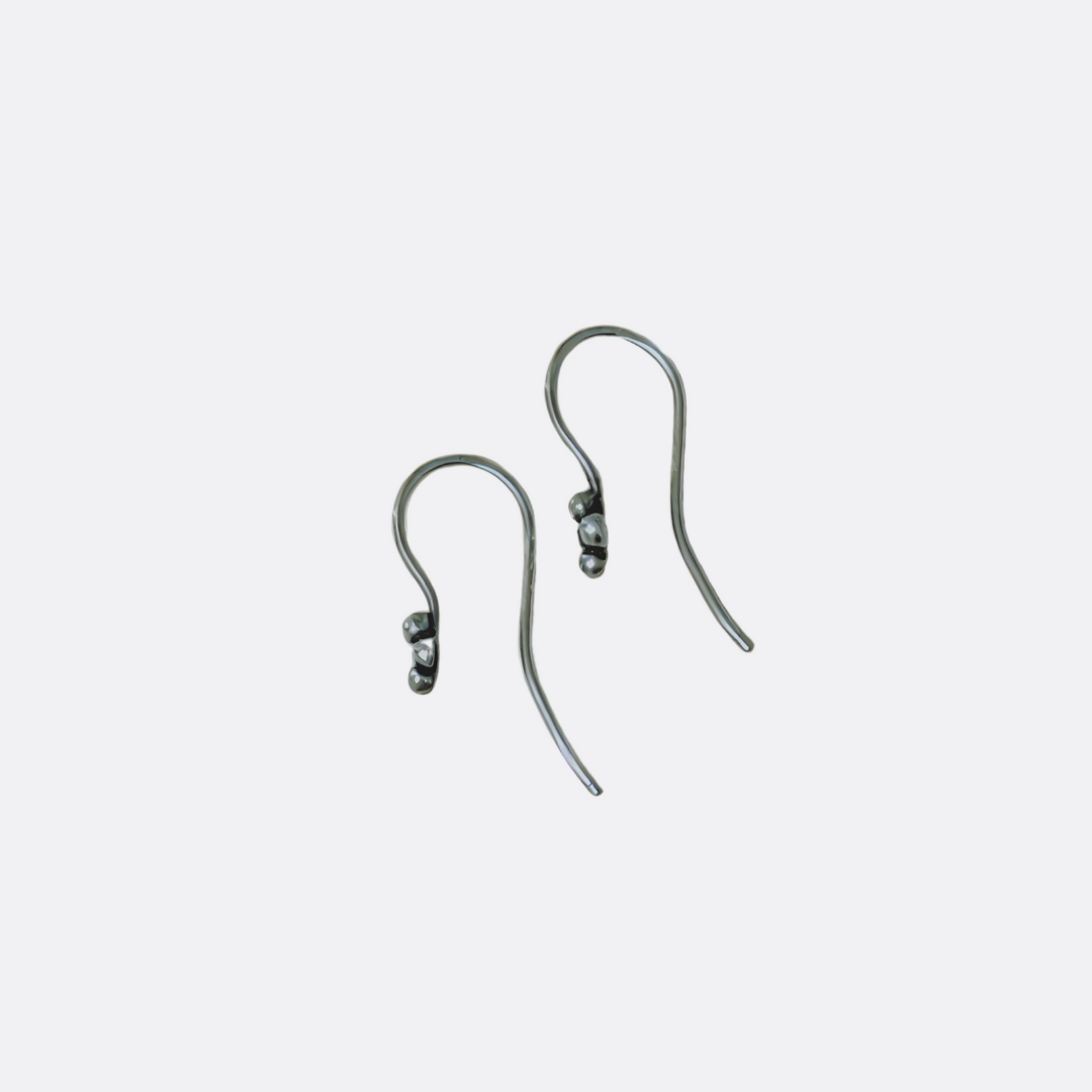 Sterling silver ear wires with four small silver balls laying on white surface board.