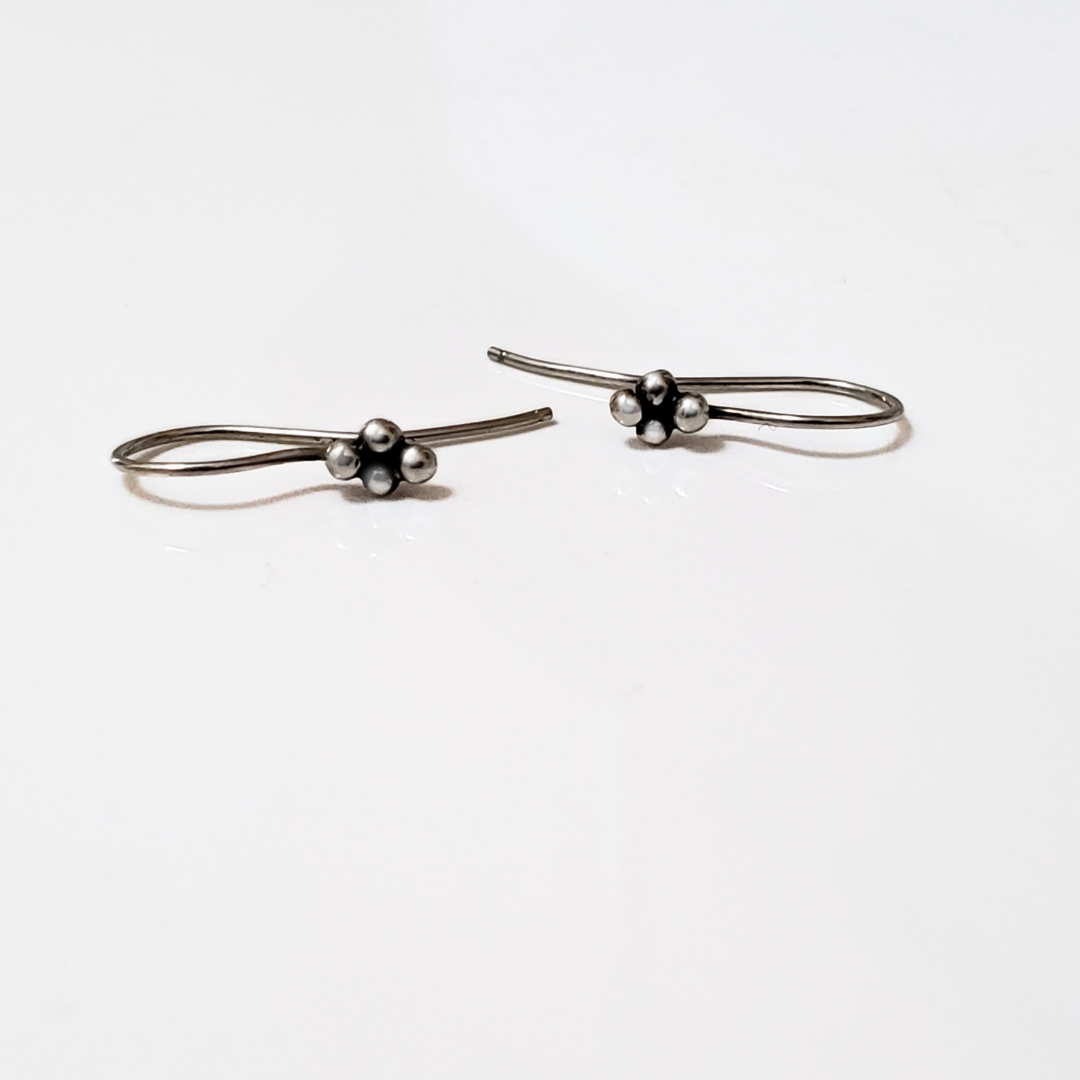Sterling silver ear wires with four small silver balls laying on white surface board.