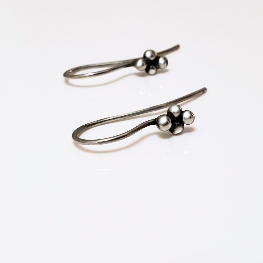 Sterling silver ear wires with four small silver balls laying on white surface board.