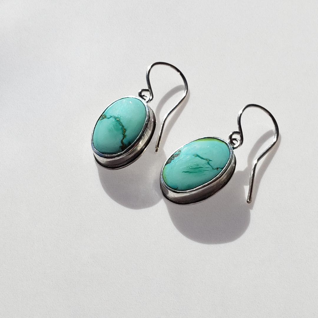 Oval turquoise earrings with silver ear wires laying on white background