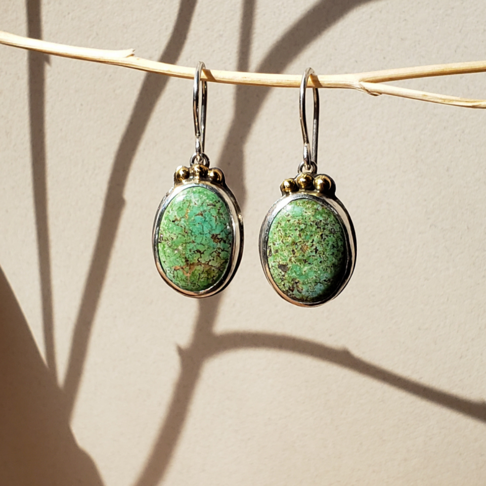 Turquoise and gold earrings against beige background