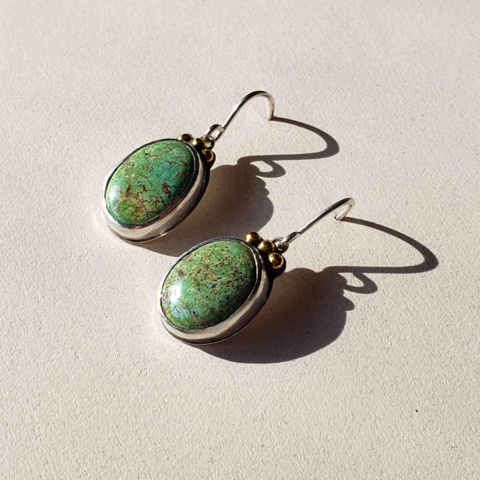 Turquoise and gold earrings against beige background