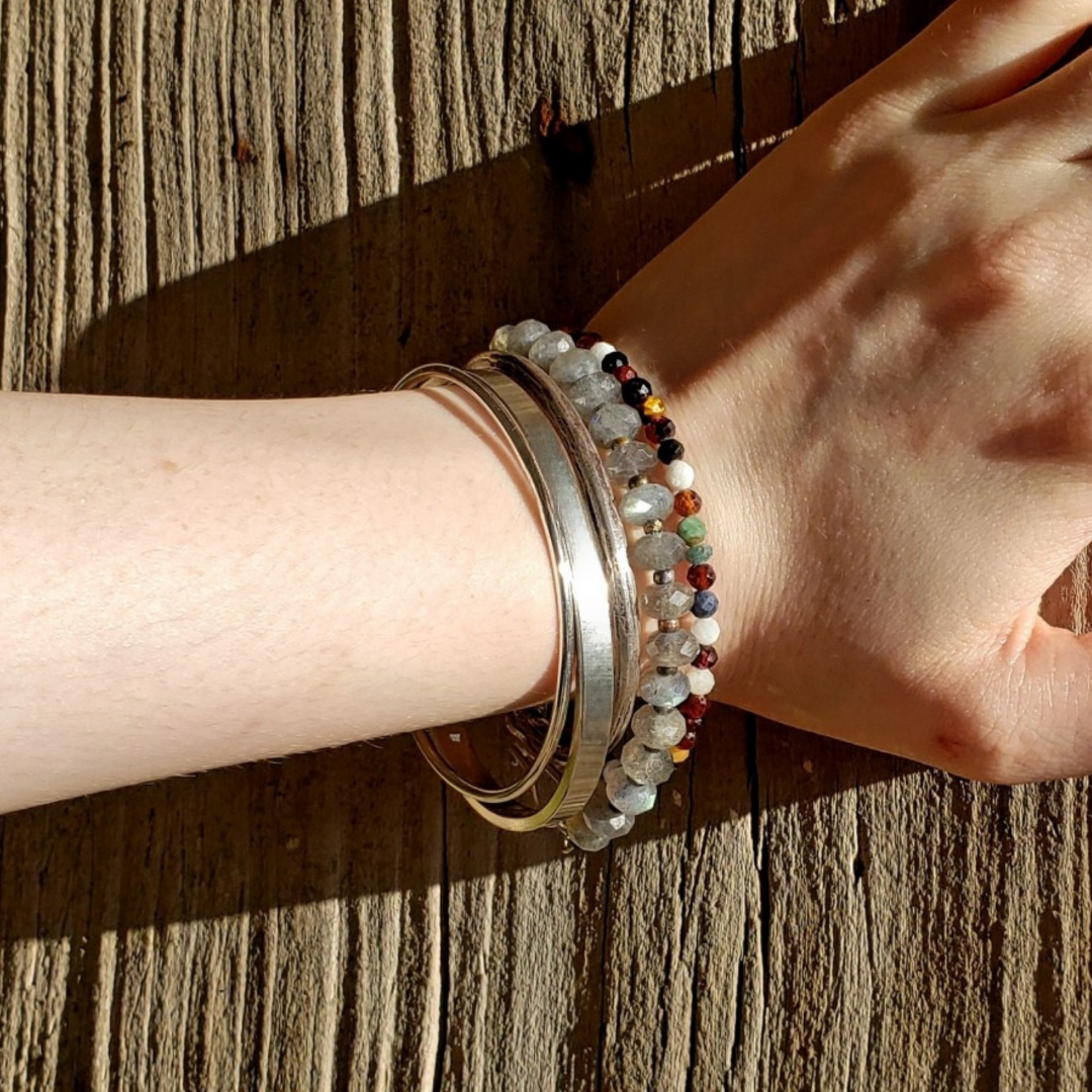Womans arm with stacked bracelet and beaded bracelet against wooden background