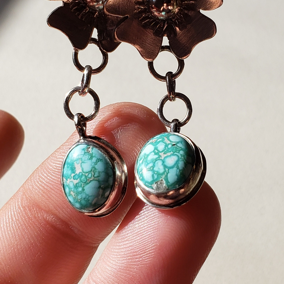 Image of a hand holding two turquoise gemstone hung from silver flower earrings
