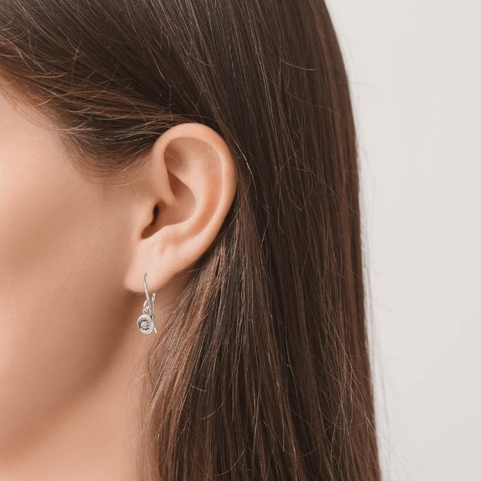 Left facing woman ear wearing small silver star earrings on silver ear wires.