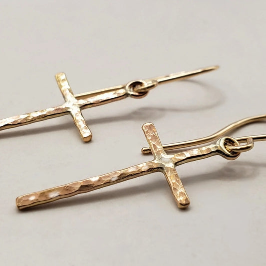 Close up image of gold cross earrings with subtle hammered texture finish hung on artisan wires