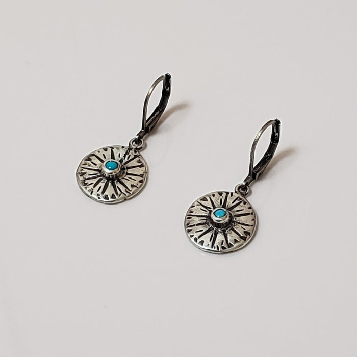 Small silver disc earrings with stamped design and blue turquoise center set against a gray background