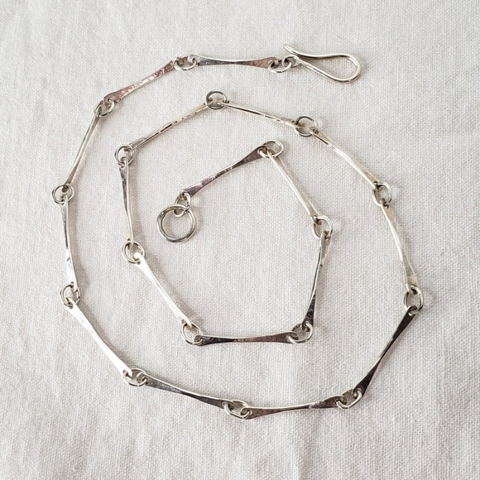 Image of large sterling silver bone chain coiled on white linen cloth