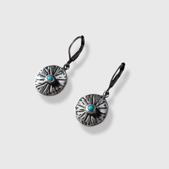 Small silver disc earrings with stamped design and blue turquoise center set against a gray background