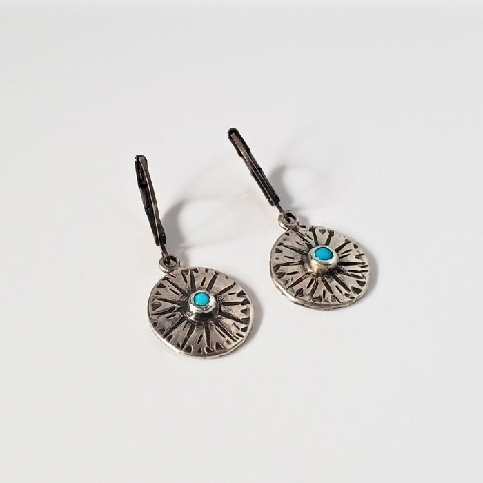 Small silver disc earrings with stamped design and blue turquoise center set against a gray background