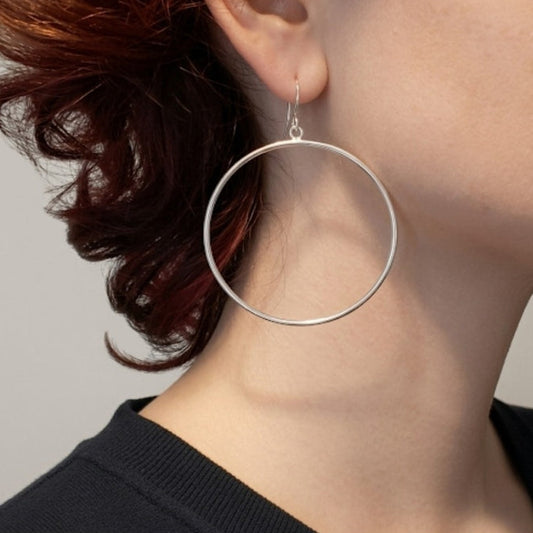 Close-up of a person wearing a silver hoop earring with a neutral background