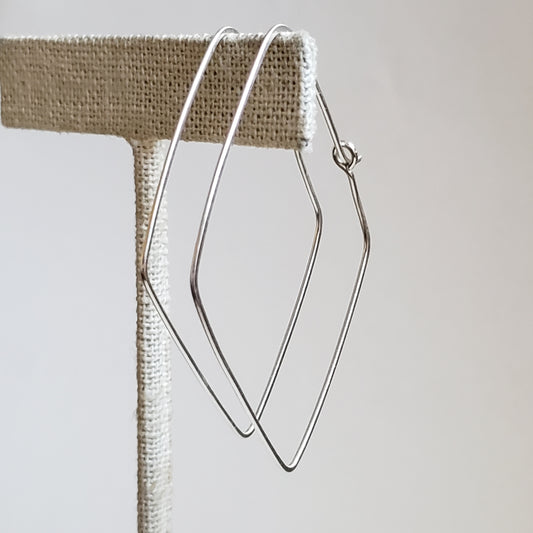 An image of a pair of large diamond shaped sterling silver hoop earrings