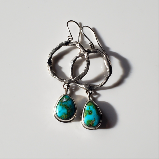 a pair of large turquoise and sterling silver hoop earrings laying on a gray background for display.