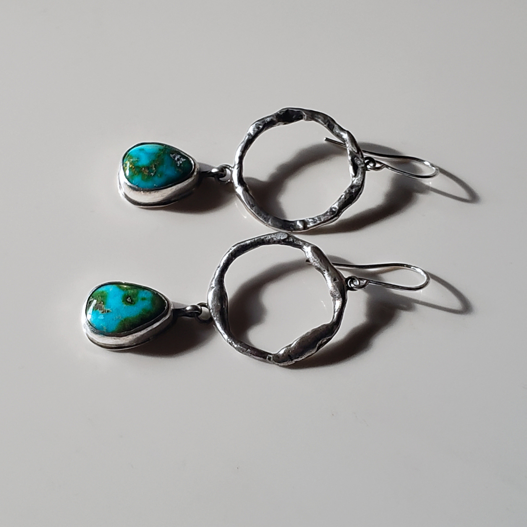 a pair of large turquoise and sterling silver hoop earrings laying on a gray background for display.