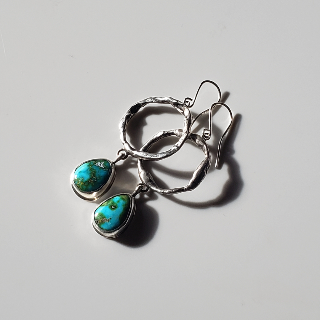 a pair of large turquoise and sterling silver hoop earrings laying on a gray background for display.