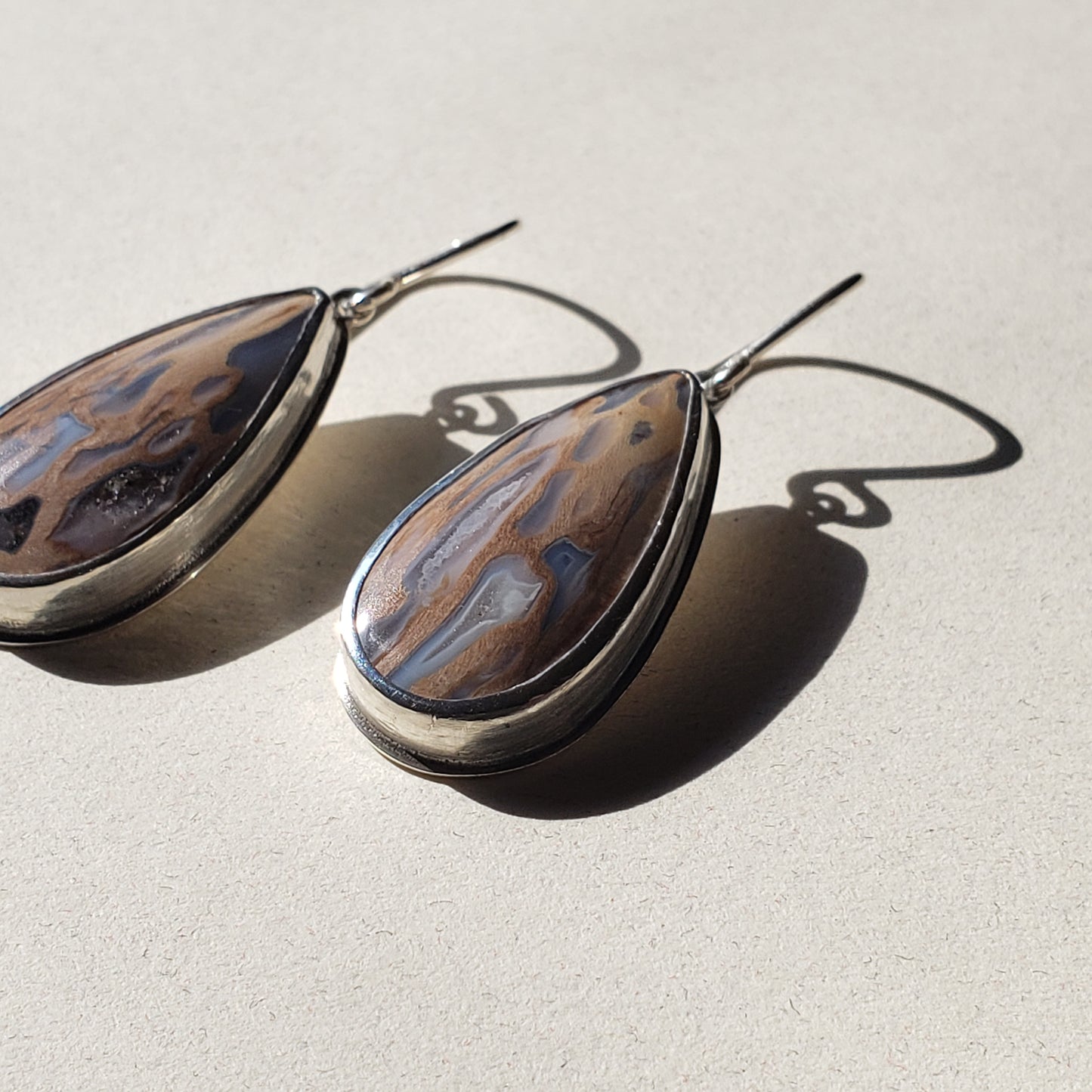 Image of large teardrop fossil earrings against beige background