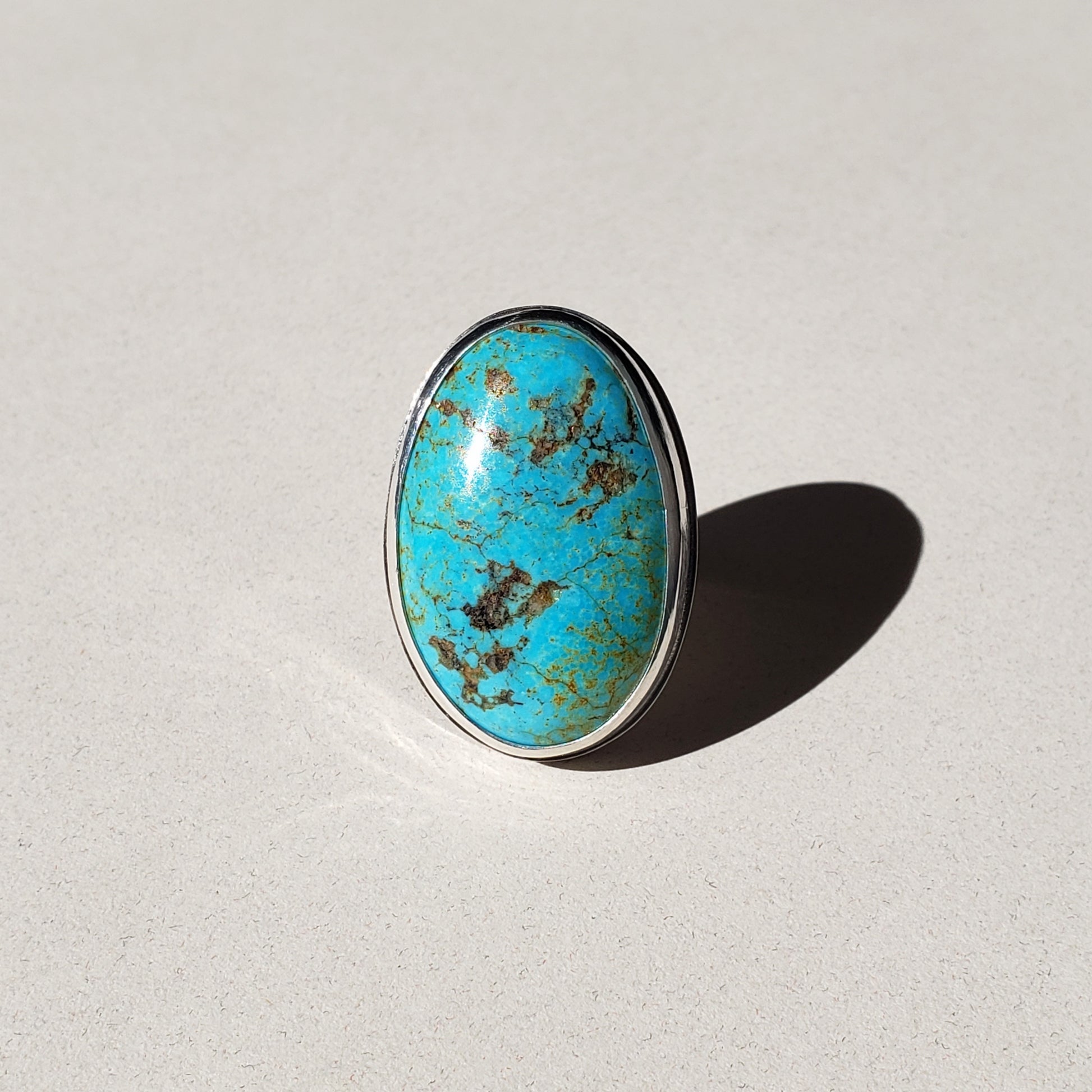 This is a large oval turquoise ring handmade from fine and sterling silvers. This turquoise statement ring is a size 7.5 and features a natural Turquoise Mountain gemstone. The ring is finished on a traditional silver band with hand hammered texture, adding a soft rustic quality to this one of a kind turquoise ring. 