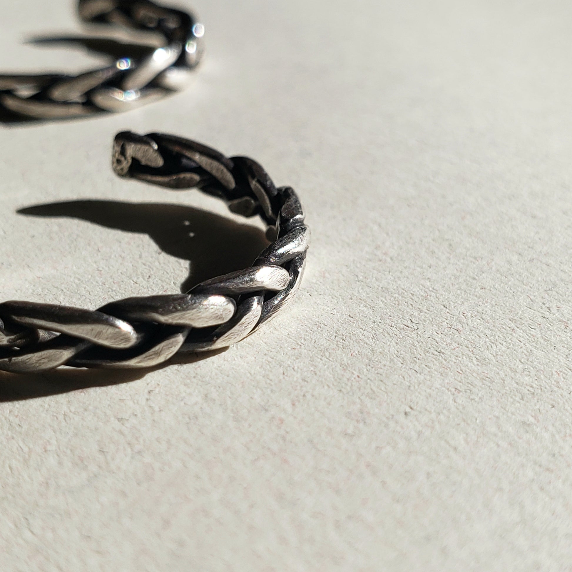 A pair of handcrafted silver hoop earrings against beige background