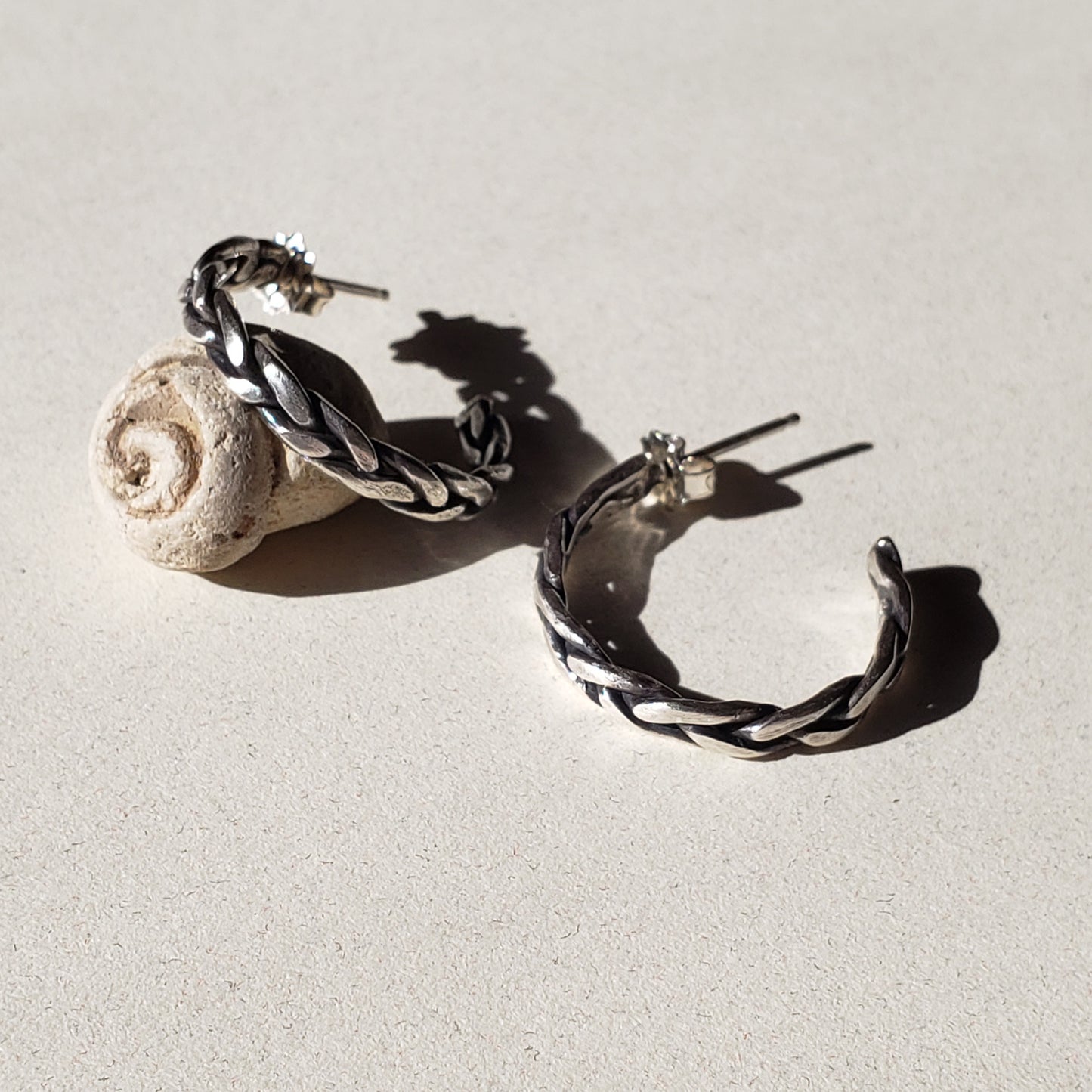 A pair of handcrafted silver hoop earrings against beige background 