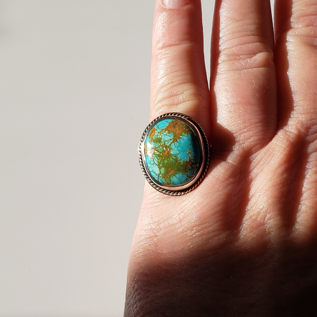 Large turquoise ring on womans hand against white background 