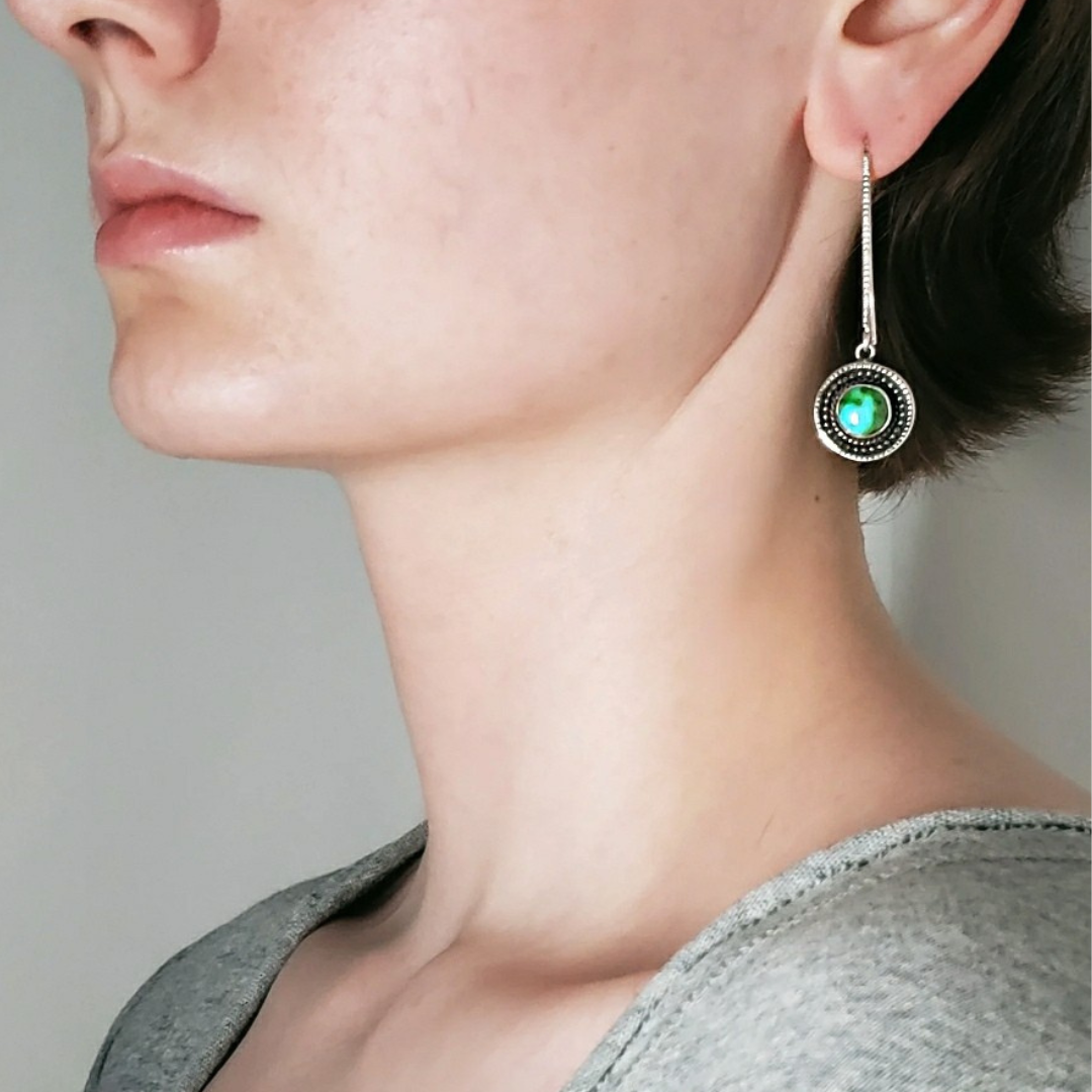 Left facing woman wearing long turquoise threader earrings against white background 