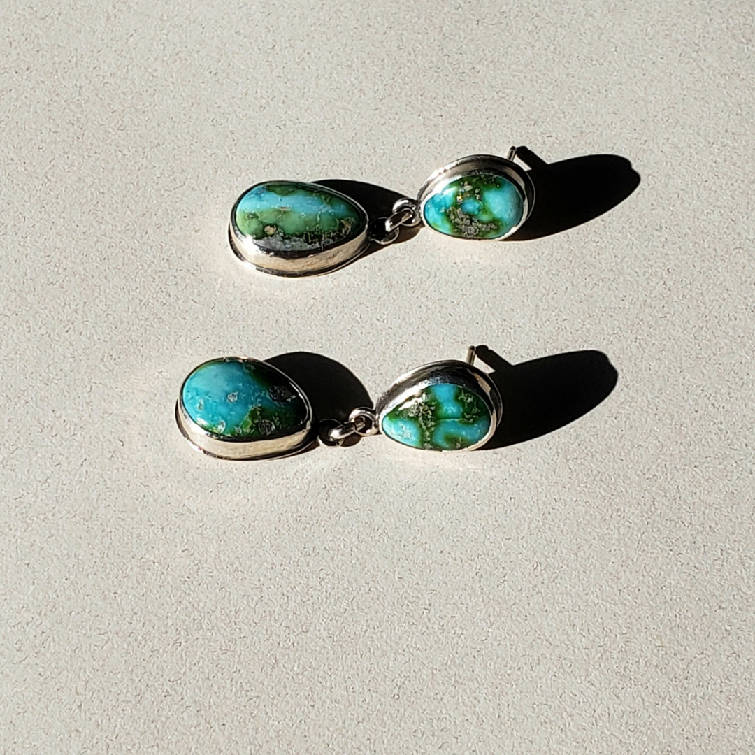 A pair of turquoise earrings laying on a white table