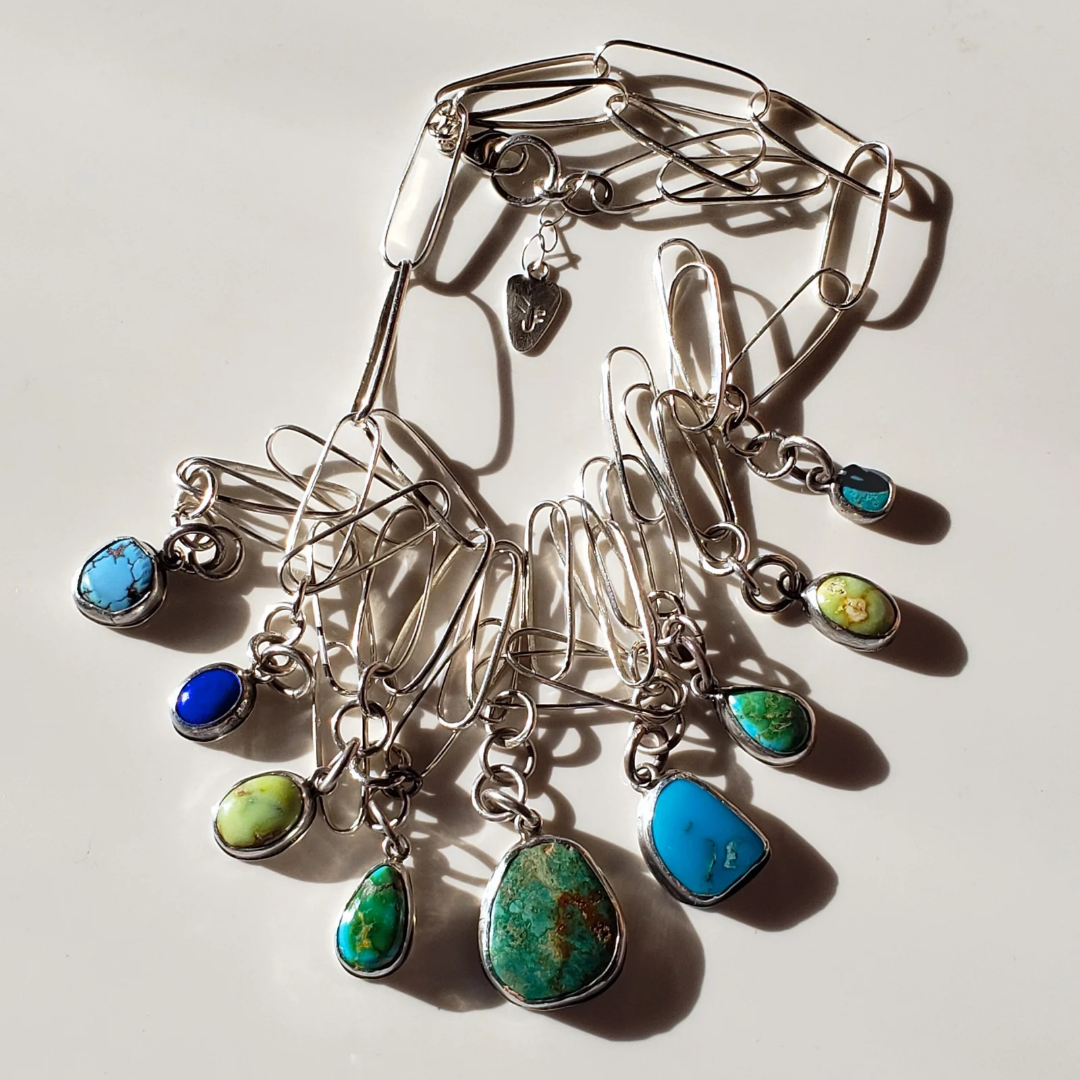 Image of colorful gemstone charm necklace against white background. This necklace has green and blue turquoise gemstone charm drops attached to a elongated sterling silver paperclip chain. 