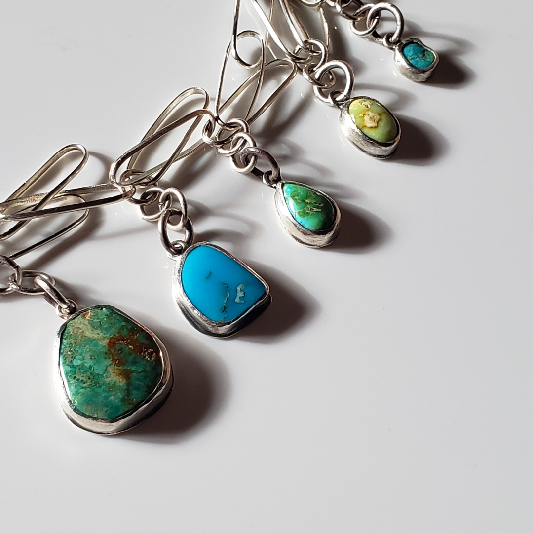 Image of colorful gemstone charm necklace against white background. This necklace has green and blue turquoise gemstone charm drops attached to a elongated sterling silver paperclip chain. 