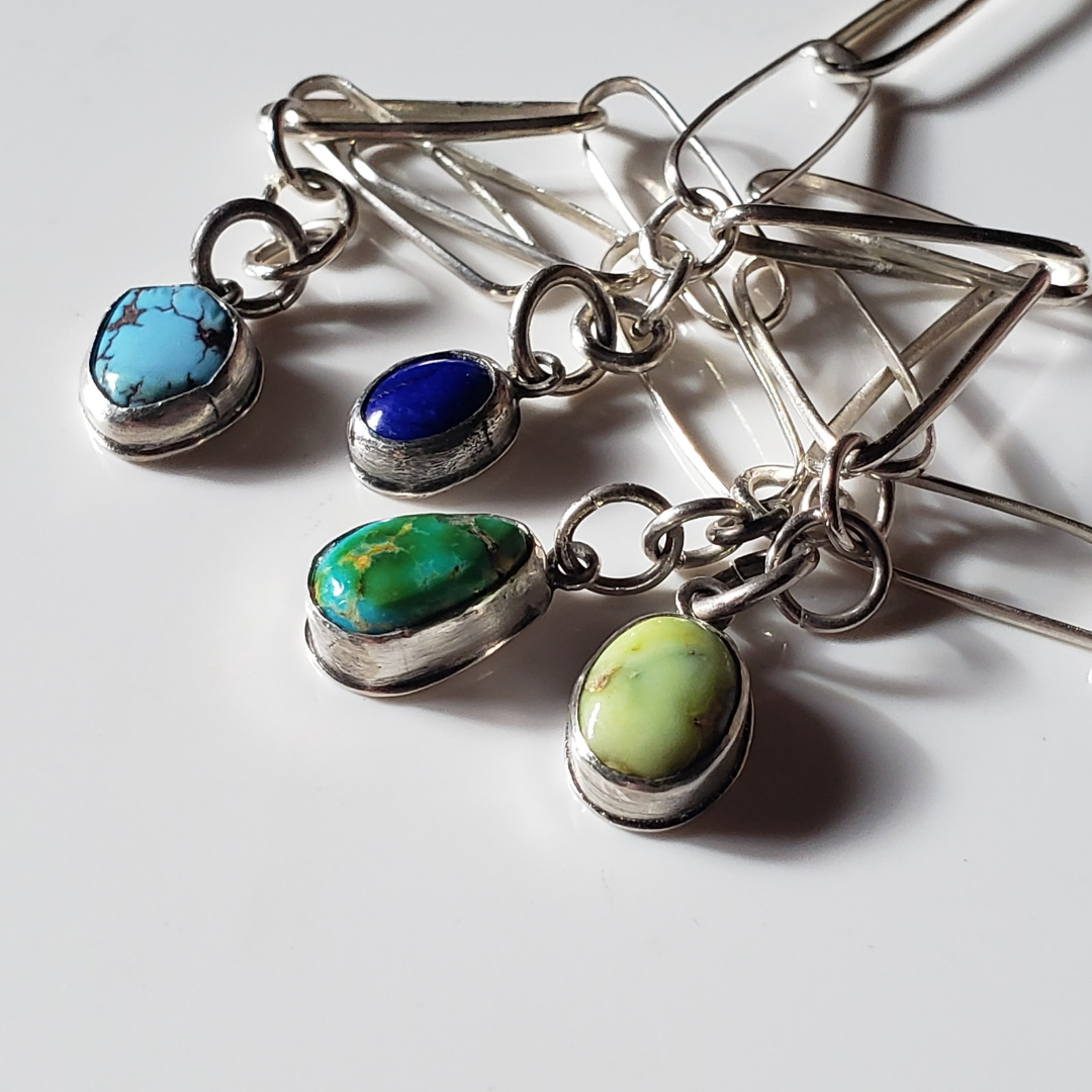 Image of colorful gemstone charm necklace against white background. This necklace has green and blue turquoise gemstone charm drops attached to a elongated sterling silver paperclip chain. 