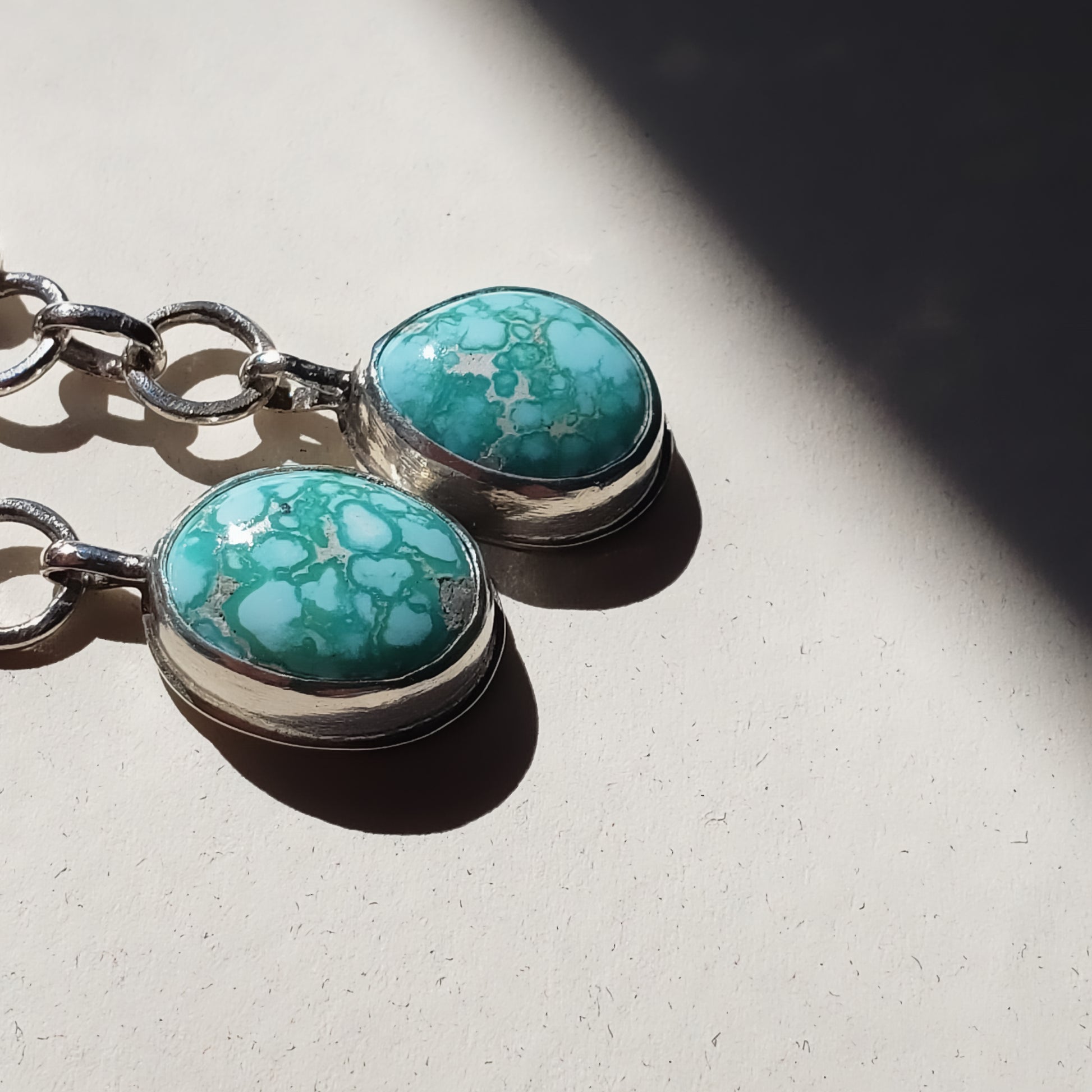 Handmade sterling silver and turquoise earrings with oval shaped, bright turquoise stones hung from large link chains from the bottom of a five petal daisy flowers tops. These earrings have sterling silver wires and are handcrafted and one of a kind earrings.