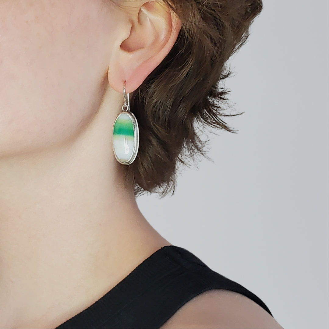 Image of woman head profile facing left wearing large green gemstone earrings 