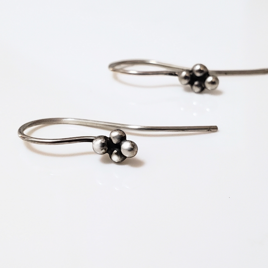 Sterling silver ear wires with four small silver balls laying on white surface board. 