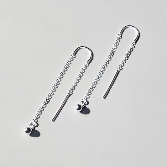 Long sterling silver threader earrings with small silver spheres left facing flat view on white surface