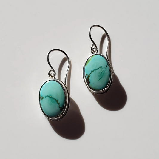 Oval turquoise earrings with silver ear wires laying on white background