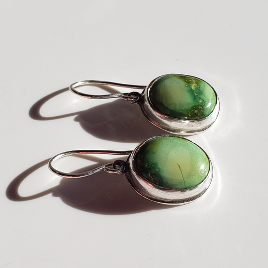 This is a image of a pair of green oval turquoise earrings on white background for display 