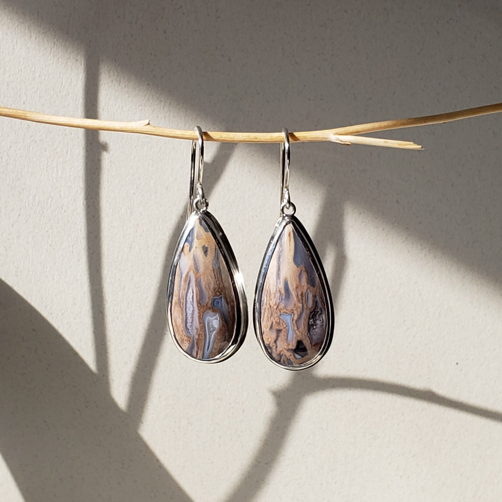 Image of large teardrop fossil earrings against beige background