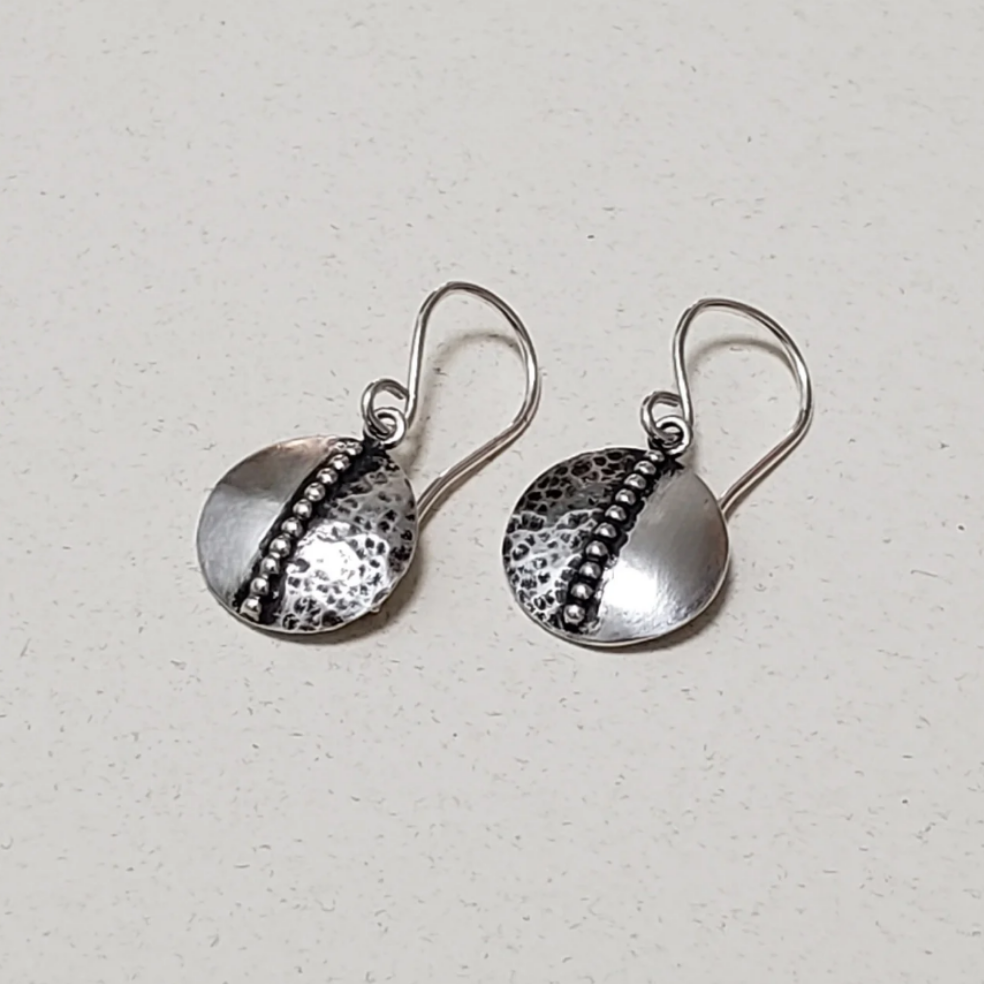 This is an image of a pair of small textured silver disc earrings. These silver disc earrings feature a half texture design, while the other half of the disc remains smooth silver. Down the center of the disc earring is a beaded accent piece, dividing the circle into two parts. These are all handcrafted silver earrings and are a featherweight style, light and easy to wear. They measure approximately half an inch in diameter and are hung from sterling wires. All handmade earrings, all sterling silver. 