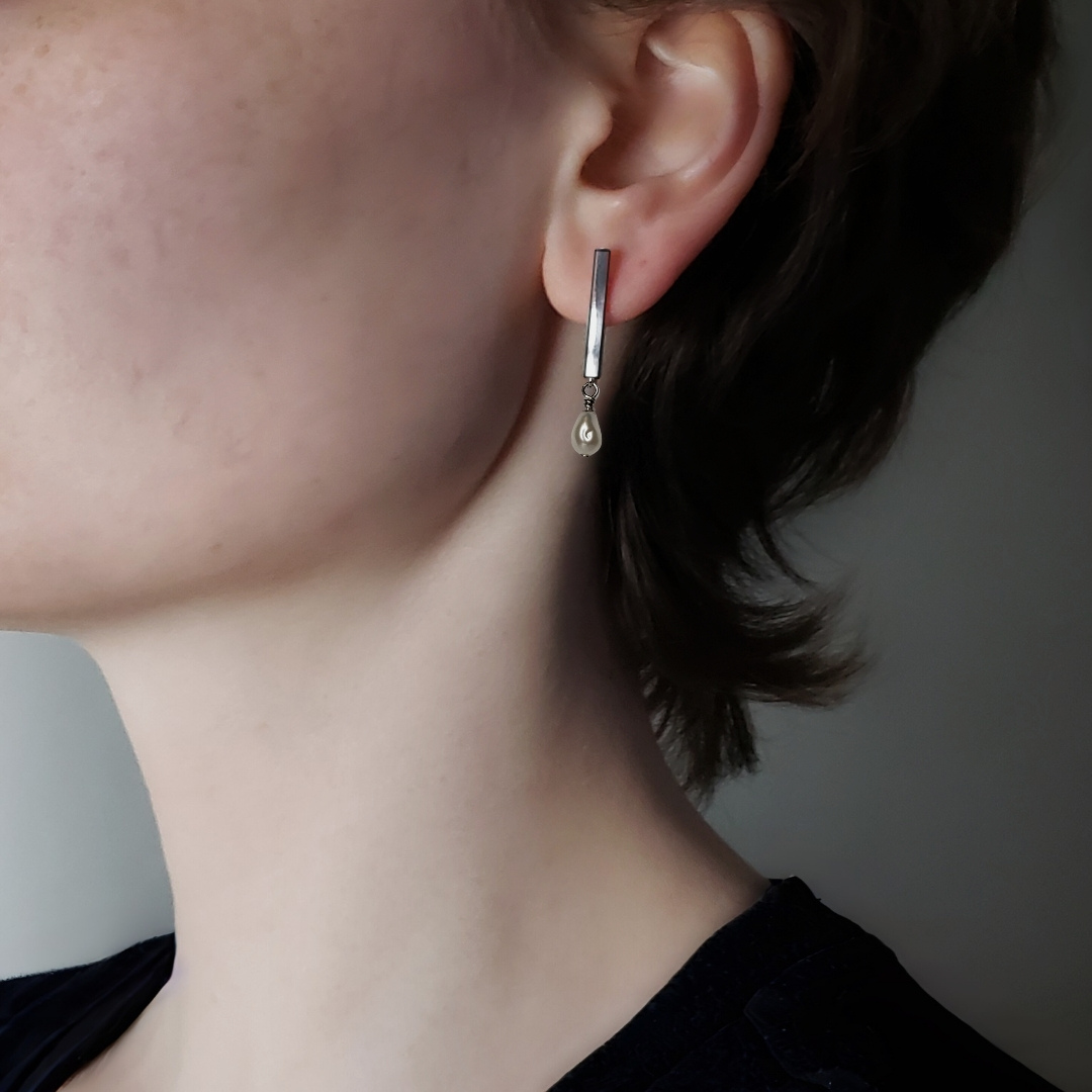 Left facing model wearing long silver bar earrings with a pearl drop 