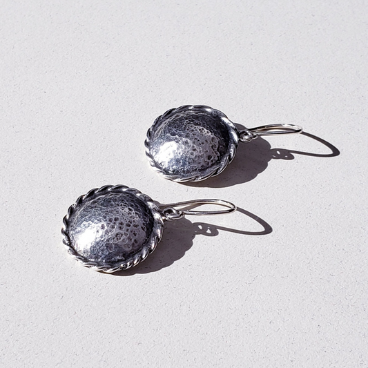 Silver disc earrings left facing on white surface