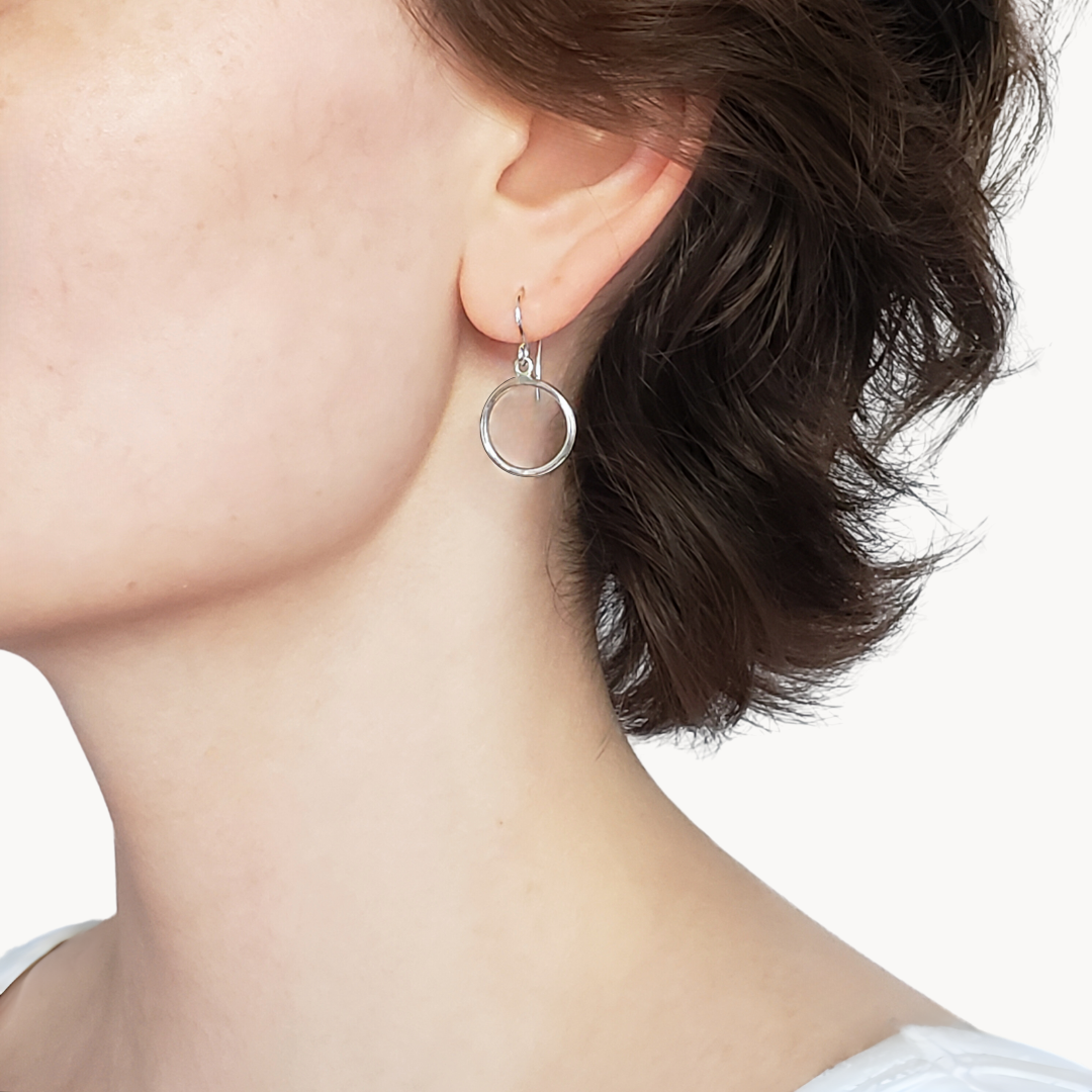 Model wearing small silver hoop earrings against white background