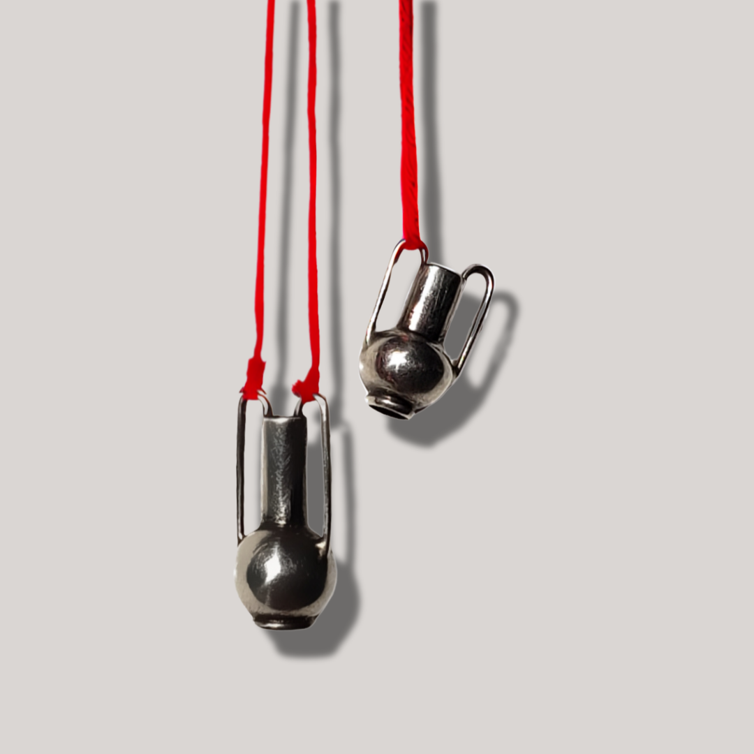 Image of two handmade sterling silver vessel pendants hanging on red string. 