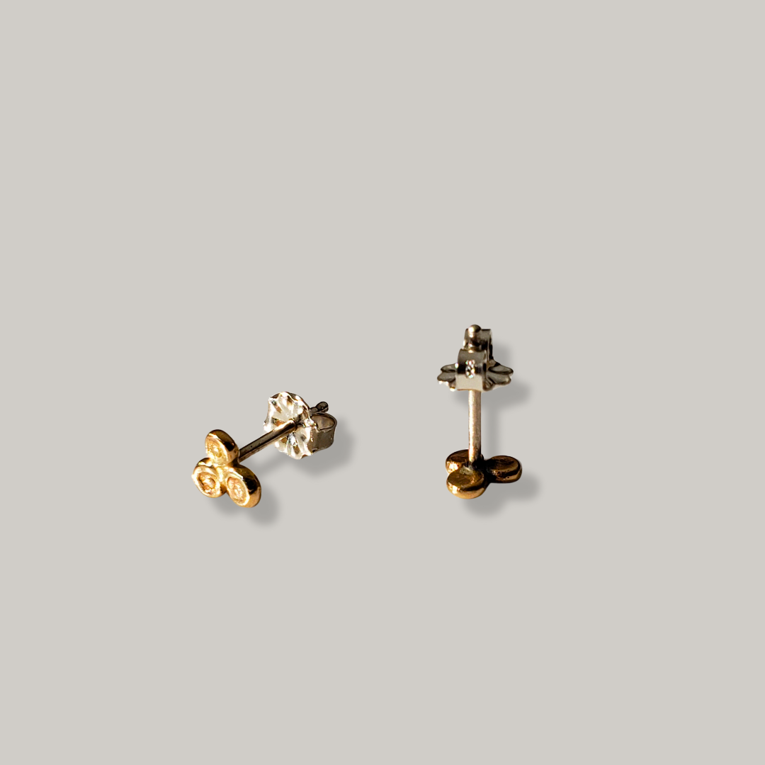 Small handmade 14k gold stud earrings with three small balls laying on a gray background 