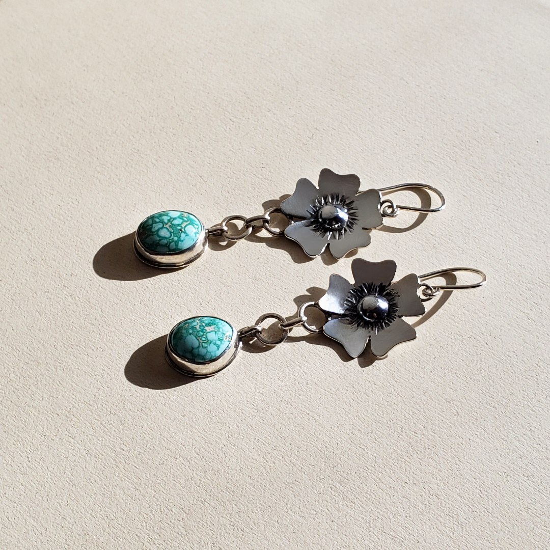 Handmade sterling silver and turquoise flower earrings with oval shaped blue turquoise stones hung from large link chains from the bottom of a five petal daisy flowers tops. These earrings have sterling silver wires and are handcrafted and one of a kind earrings.