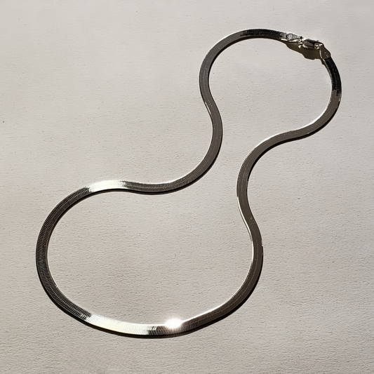 image of a wide sterling silver herringbone chain necklace against beige background 
