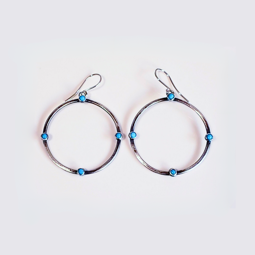 Image of sterling silver hoop earrings with small turquoise gemstones. Hoop earrings are laying on white board for display. 